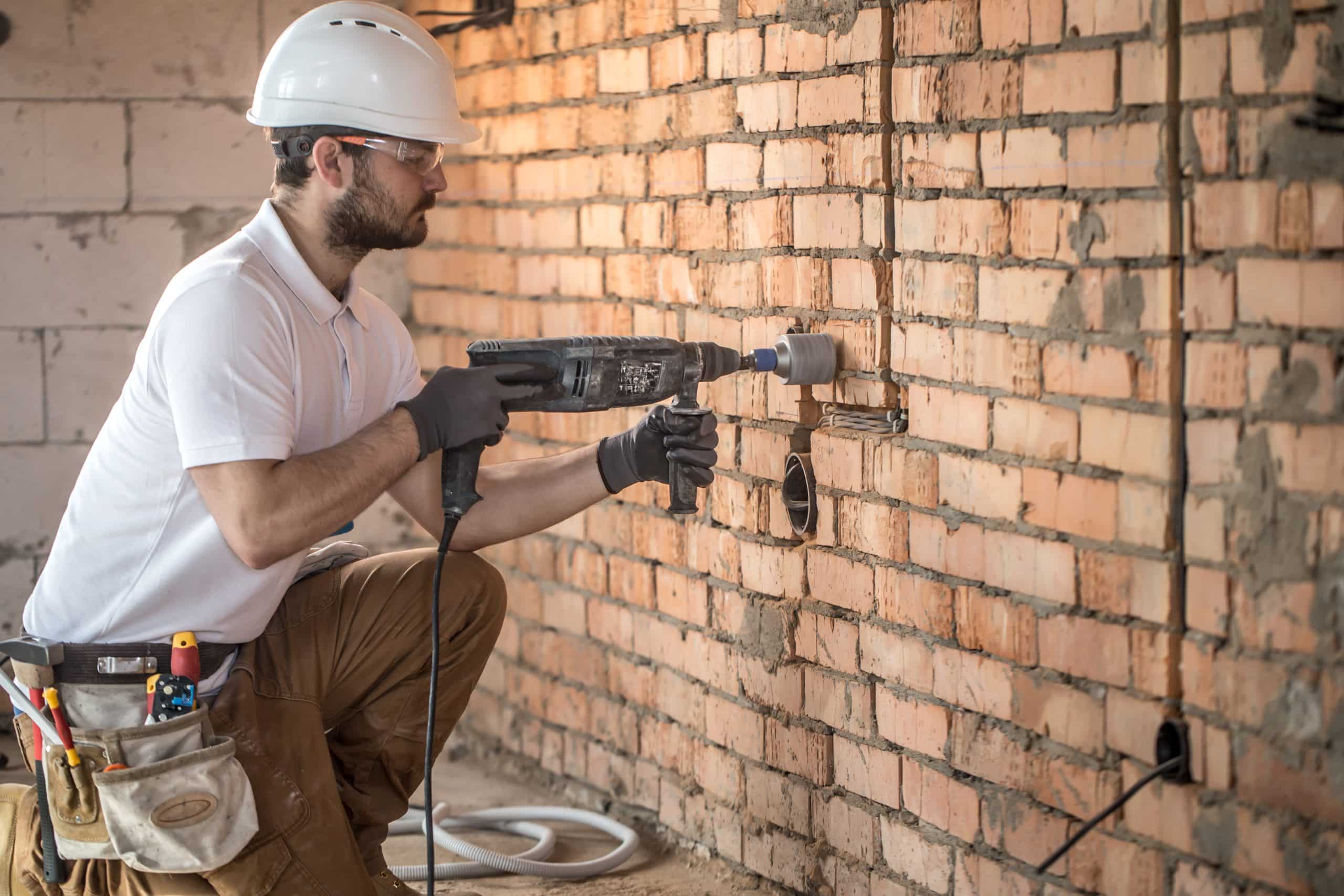 Handyman uses jackhammer, for installation, professional worker on the construction site. The concept of electrician and handyman. CIS Payroll Leeds