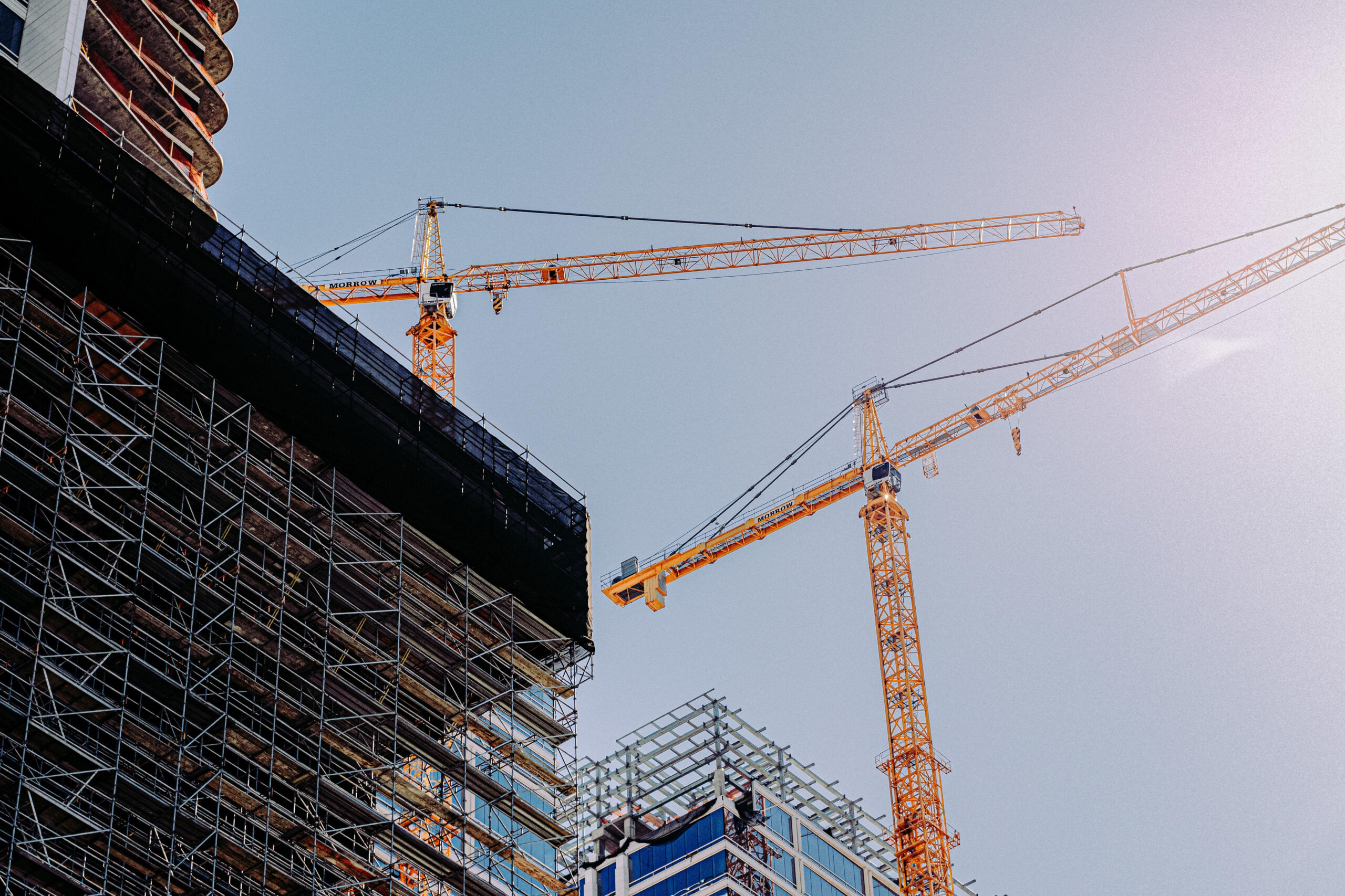 Low angle of two cranes in a construction site under a clear sky background