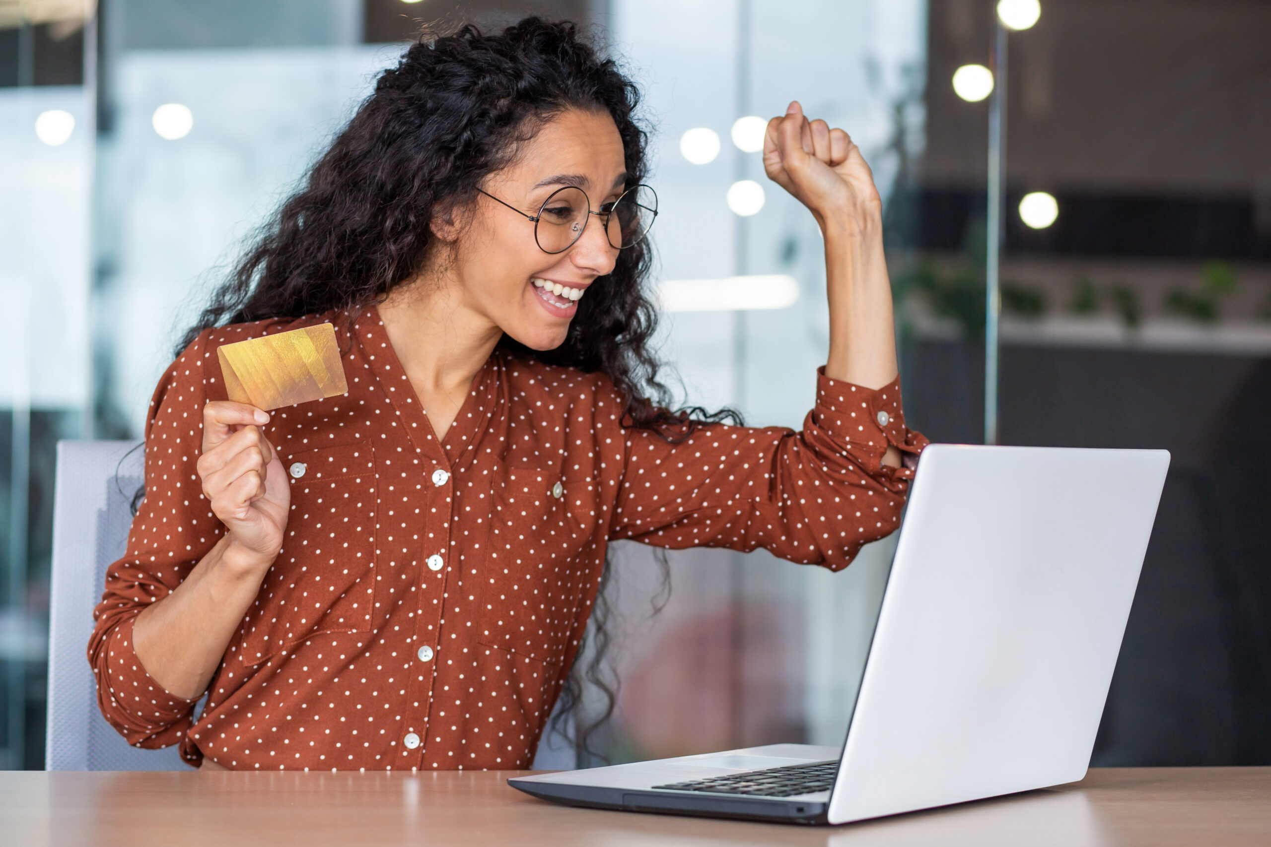 Happy joyful woman bought bargain online product with discount, business woman celebrating successful online shopping at workplace inside office, holding bank credit card, using laptop