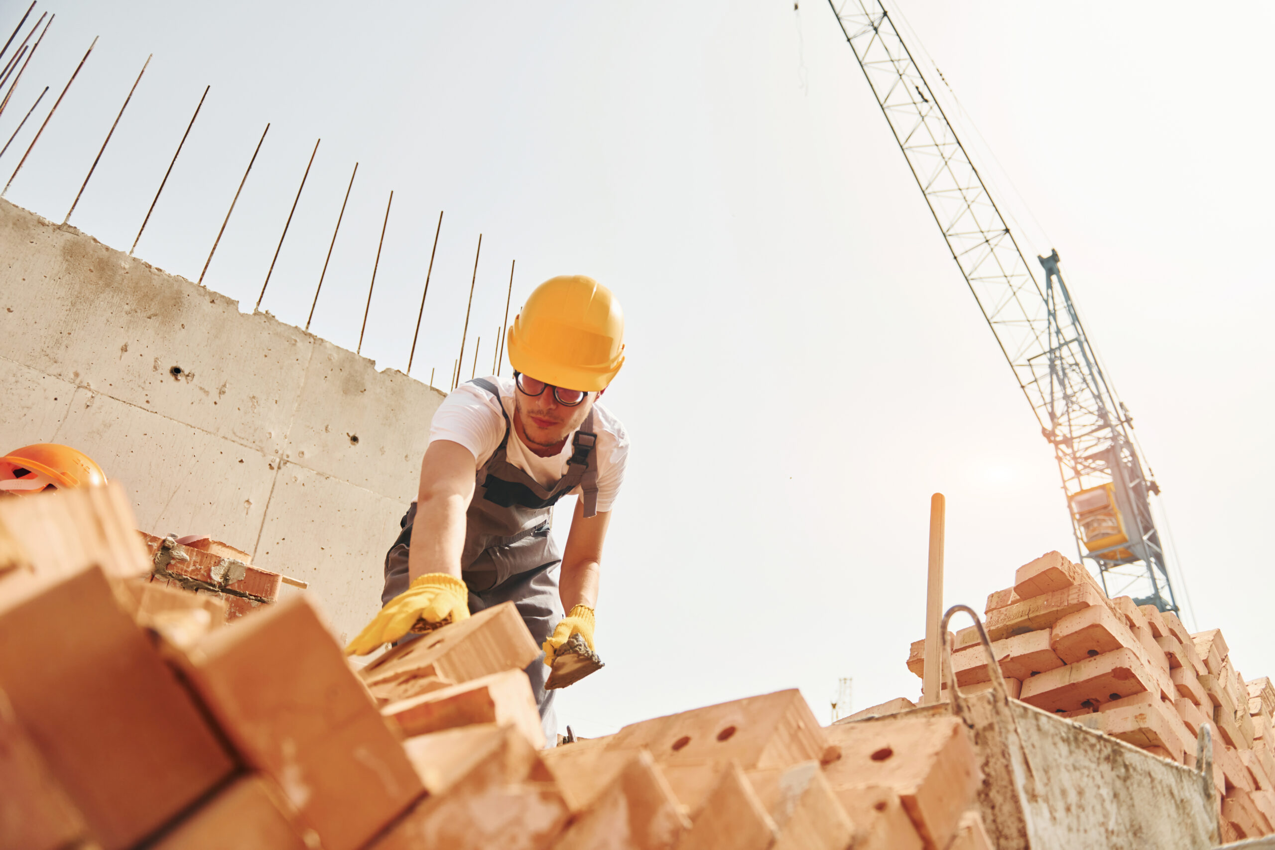 Using bricks. Young construction worker in uniform is busy at the unfinished building